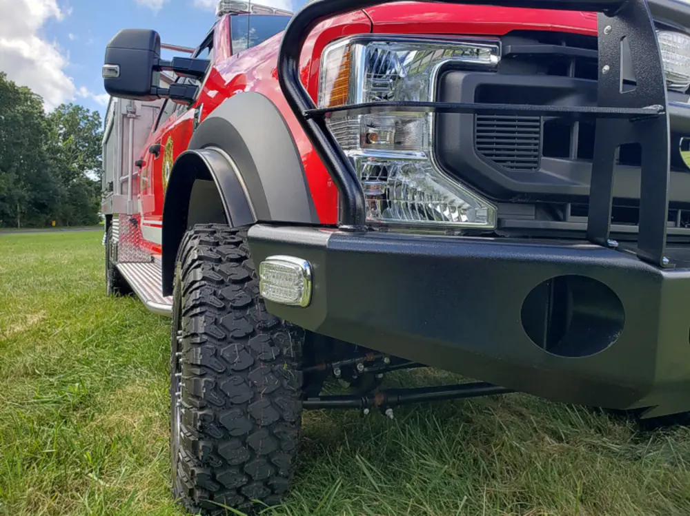 Exterior view of small fire truck showing cab, body compartments, and wheel/tire area.