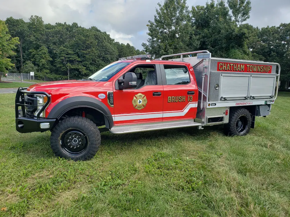 Exterior view of small fire truck showing cab, body compartments, and wheel/tire area.