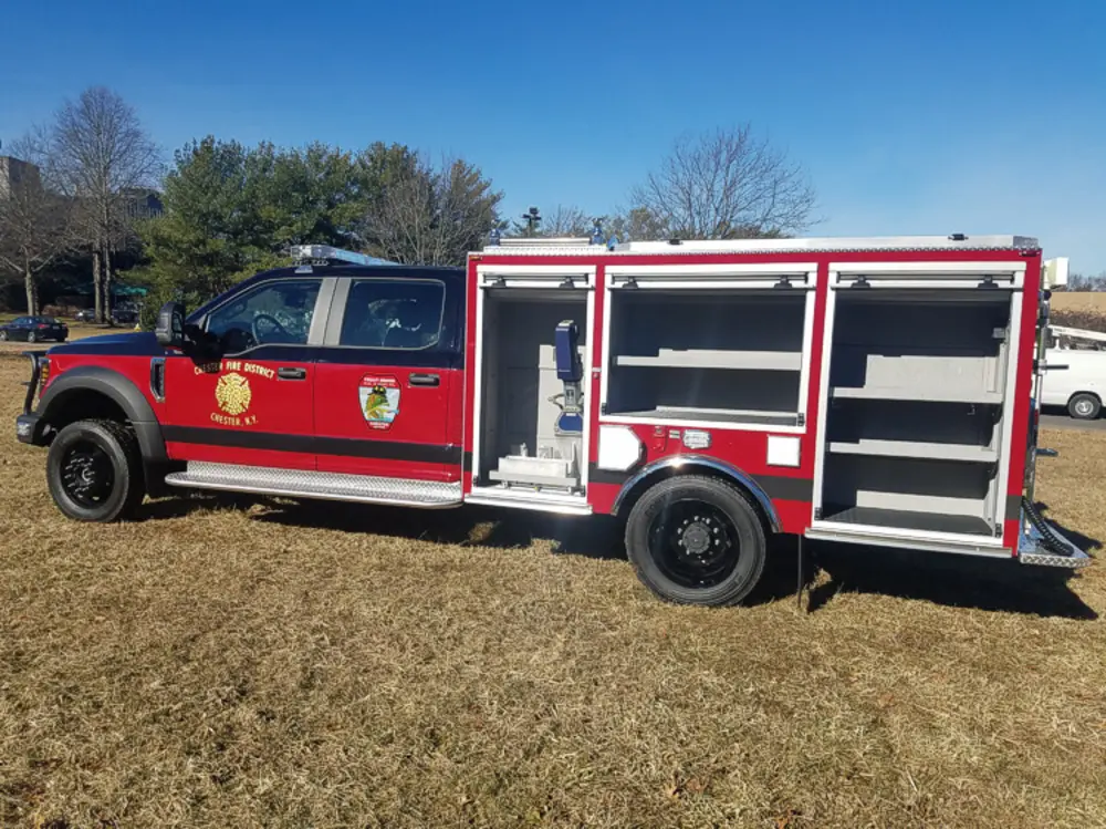 Exterior view of small fire truck showing cab, body compartments, and wheel/tire area.