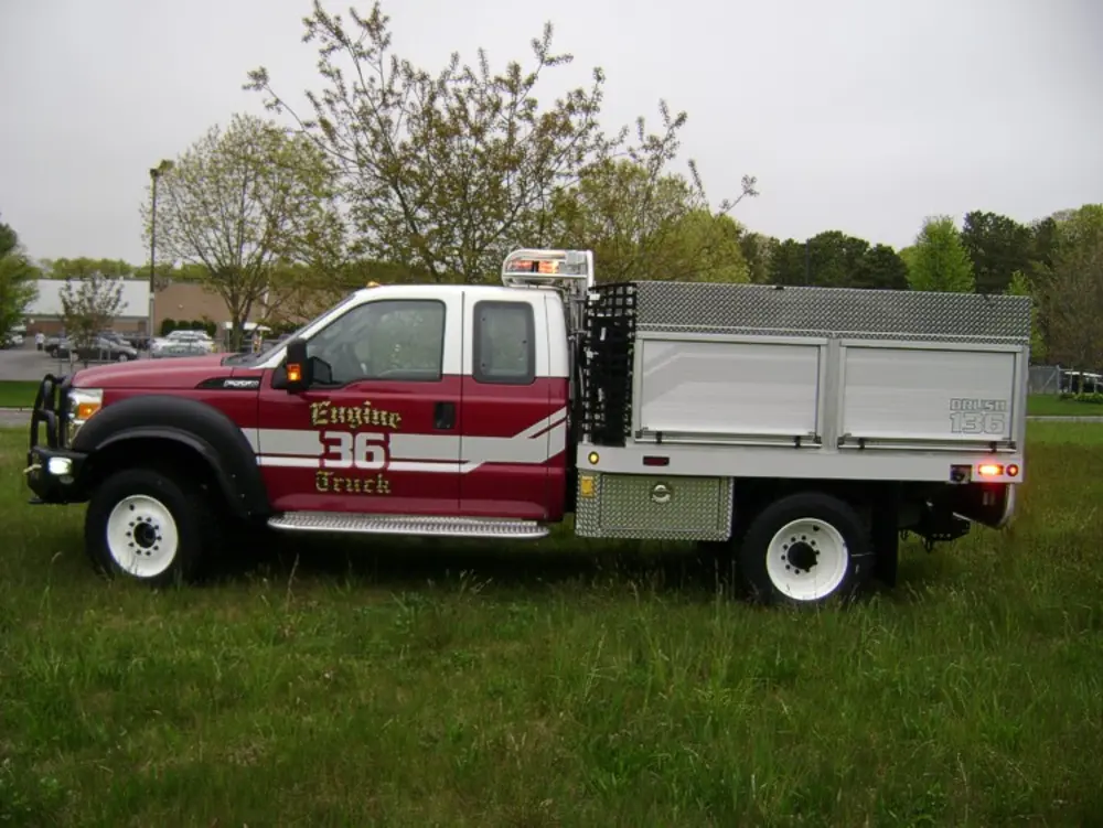Exterior view of small fire truck showing cab, body compartments, and wheel/tire area.