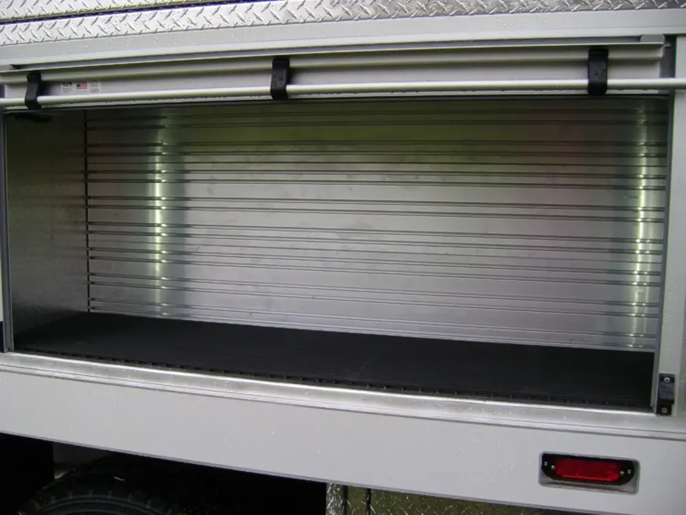 Exterior view of small fire truck showing cab, body compartments, and wheel/tire area.