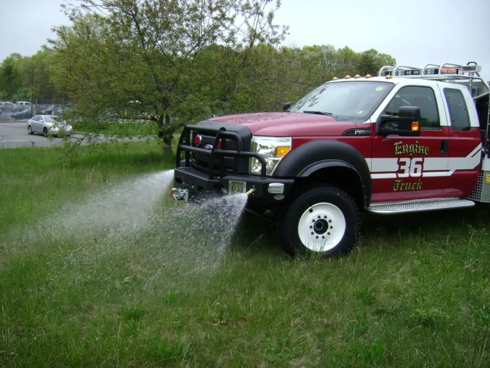 Exterior view of small fire truck showing cab, body compartments, and wheel/tire area.