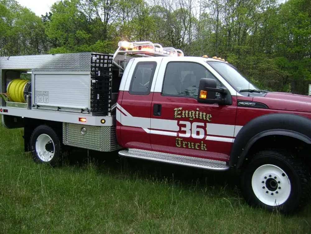 Exterior view of small fire truck showing cab, body compartments, and wheel/tire area.
