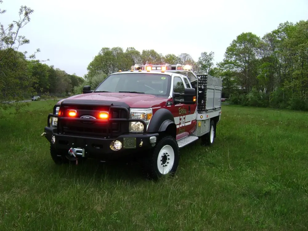 Exterior view of small fire truck showing cab, body compartments, and wheel/tire area.
