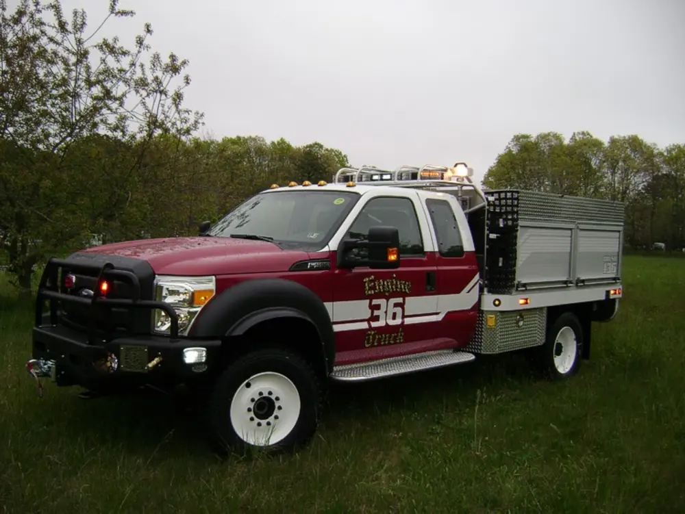 Exterior view of small fire truck showing cab, body compartments, and wheel/tire area.