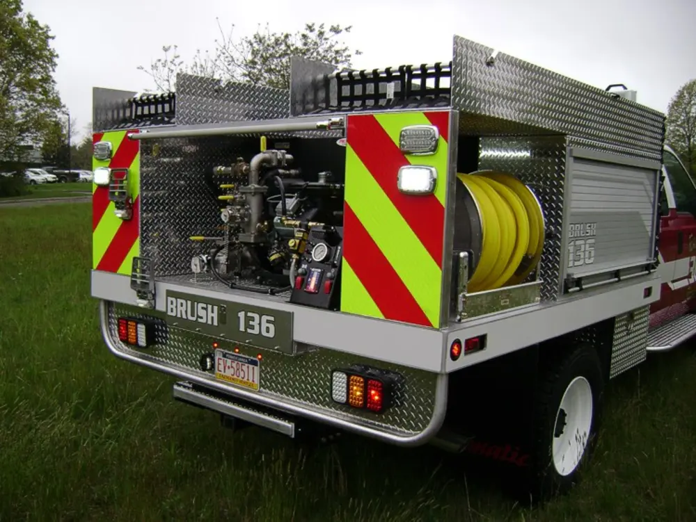 Exterior view of small fire truck showing cab, body compartments, and wheel/tire area.