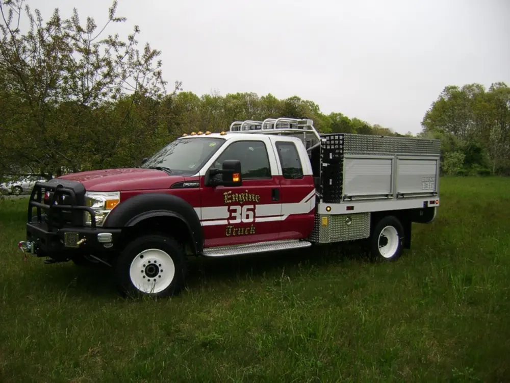 Exterior view of small fire truck showing cab, body compartments, and wheel/tire area.