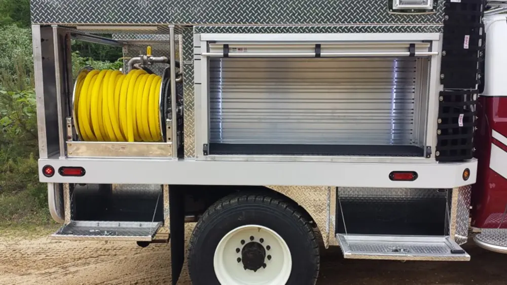 Exterior view of small fire truck showing cab, body compartments, and wheel/tire area.