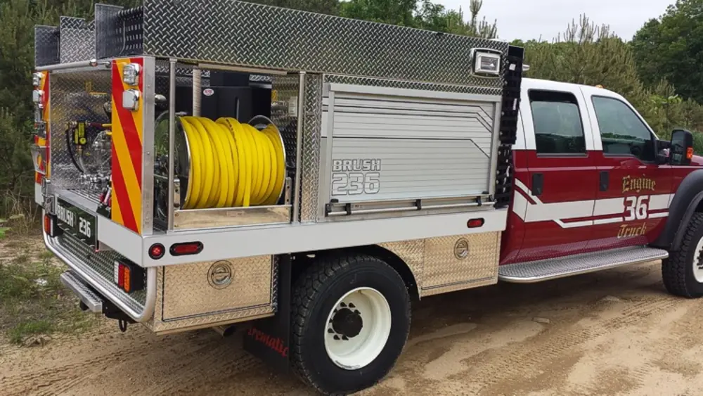 Exterior view of small fire truck showing cab, body compartments, and wheel/tire area.