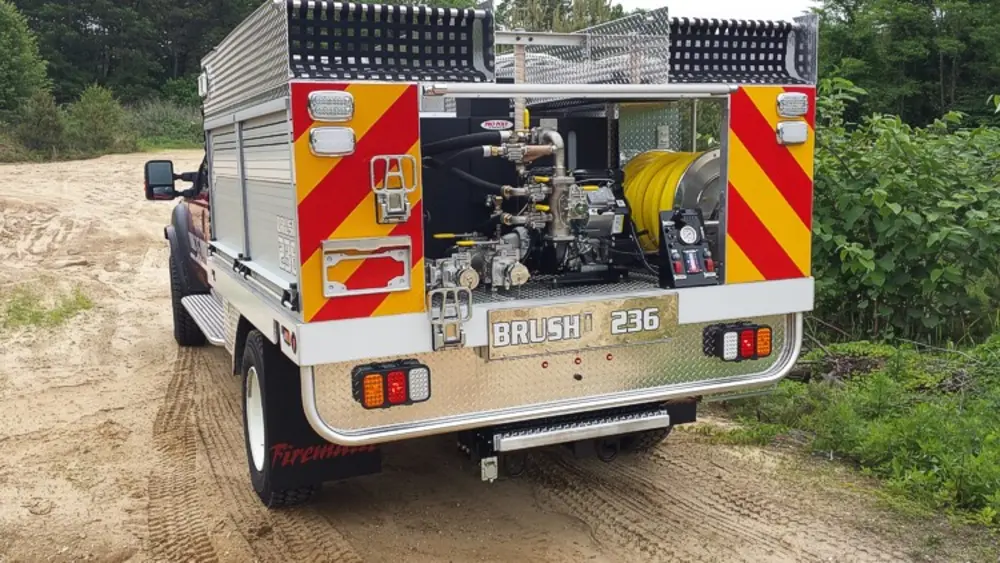 Exterior view of small fire truck showing cab, body compartments, and wheel/tire area.