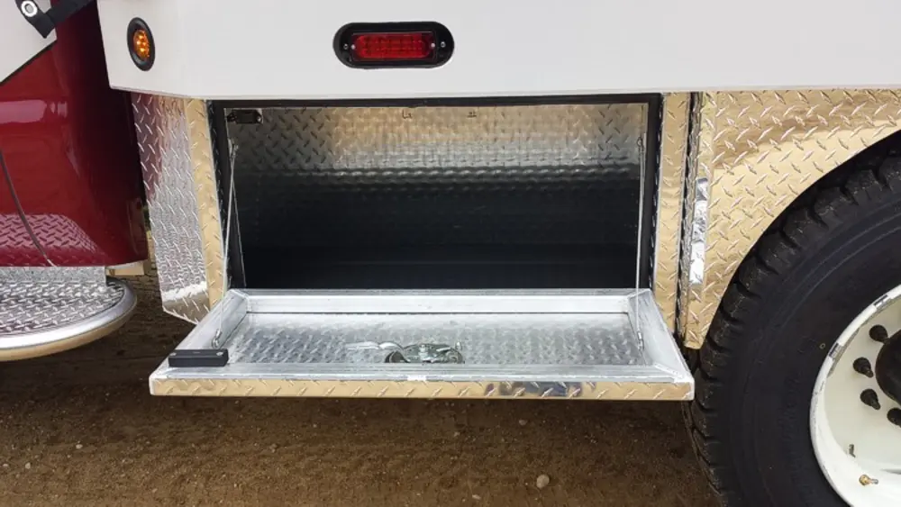 Exterior view of small fire truck showing cab, body compartments, and wheel/tire area.