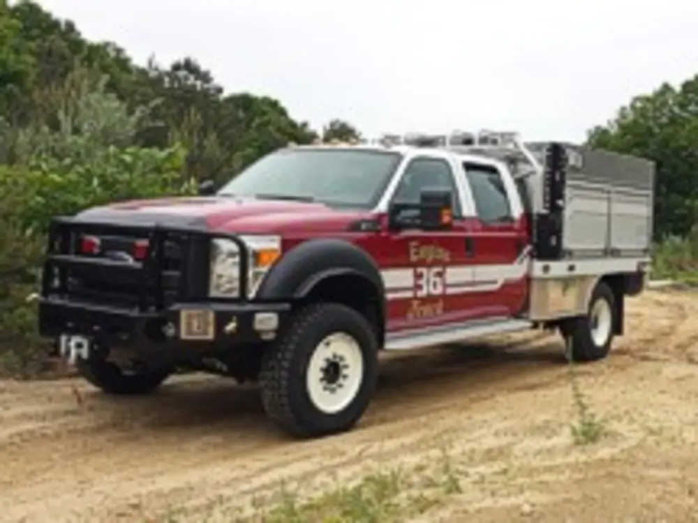 Exterior view of small fire truck showing cab, body compartments, and wheel/tire area.