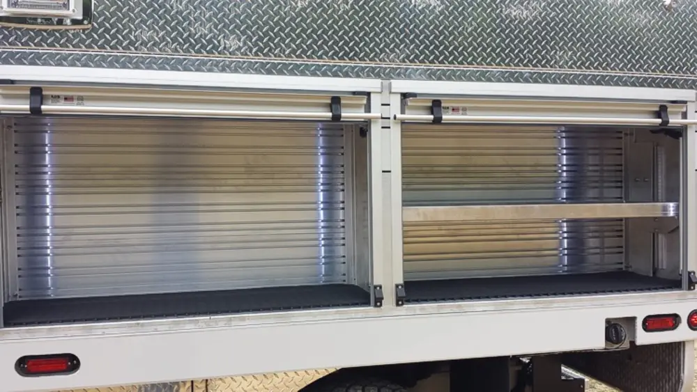 Exterior view of small fire truck showing cab, body compartments, and wheel/tire area.