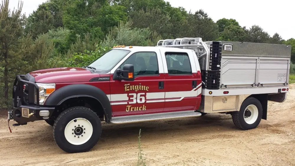 Exterior view of small fire truck showing cab, body compartments, and wheel/tire area.
