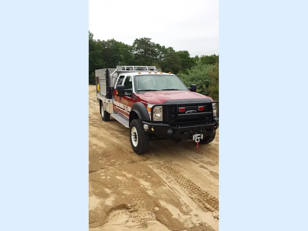 Exterior view of small fire truck showing cab, body compartments, and wheel/tire area.