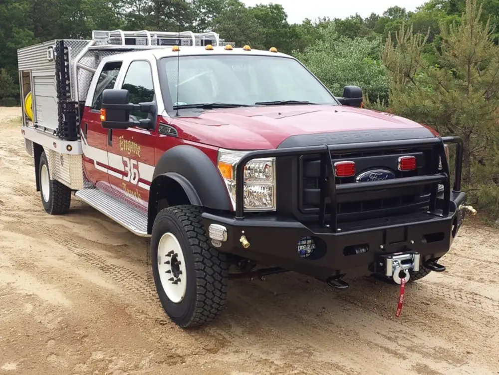 Exterior view of small fire truck showing cab, body compartments, and wheel/tire area.