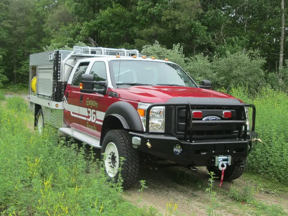 Exterior view of small fire truck showing cab, body compartments, and wheel/tire area.