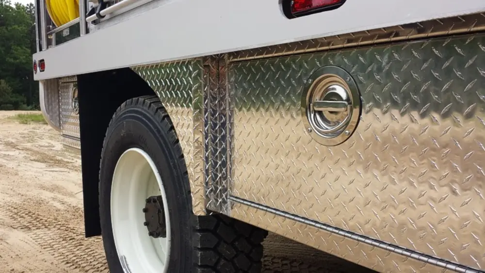 Exterior view of small fire truck showing cab, body compartments, and wheel/tire area.
