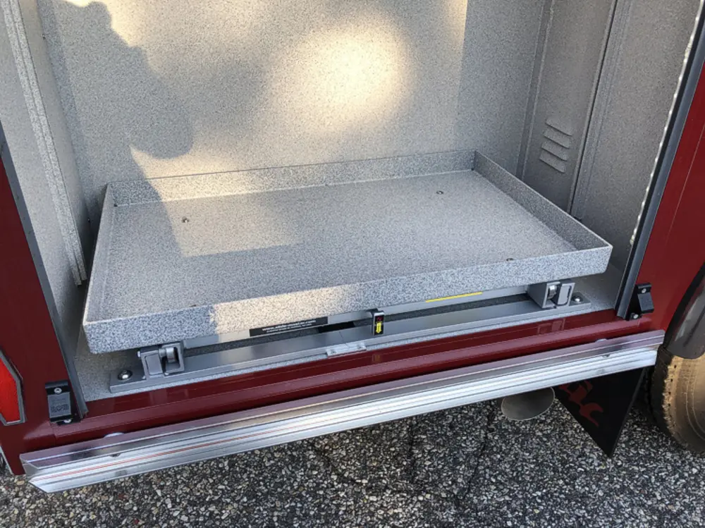 Exterior view of small fire truck showing cab, body compartments, and wheel/tire area.