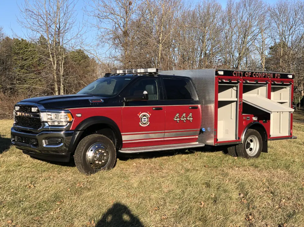 Exterior view of small fire truck showing cab, body compartments, and wheel/tire area.