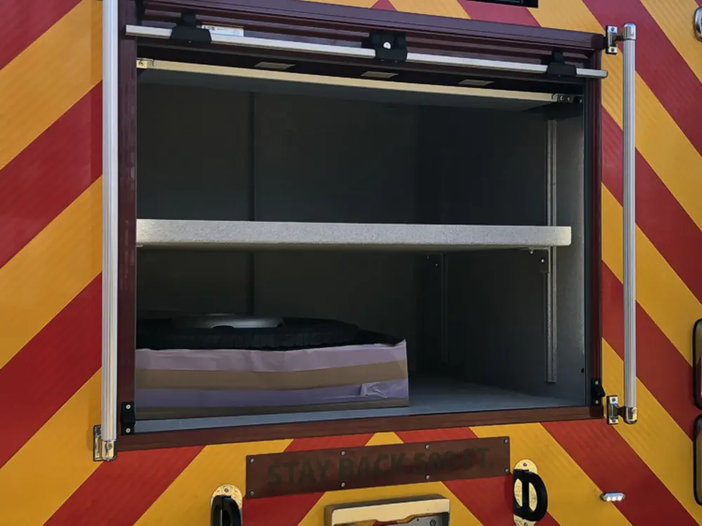 Exterior view of small fire truck showing cab, body compartments, and wheel/tire area.