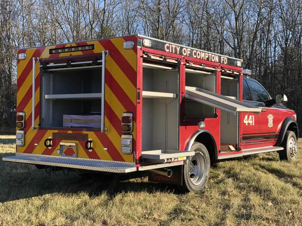 Exterior view of small fire truck showing cab, body compartments, and wheel/tire area.