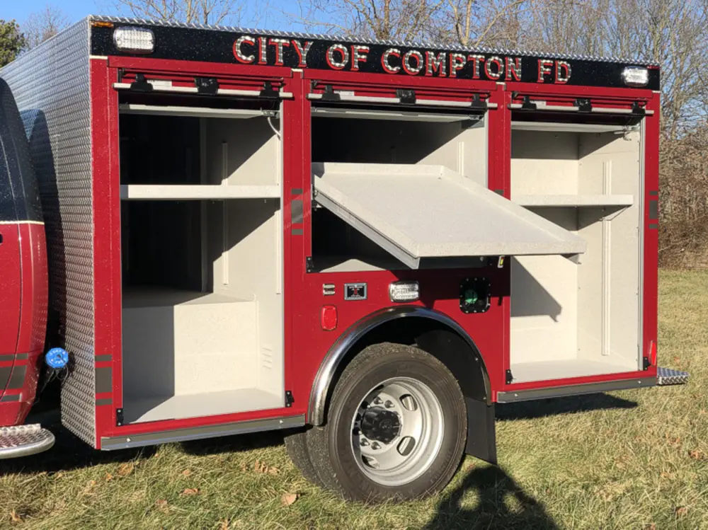 Exterior view of small fire truck showing cab, body compartments, and wheel/tire area.