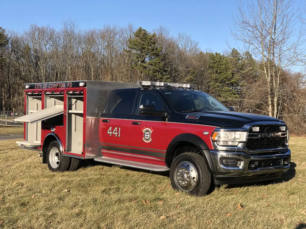 Exterior view of small fire truck showing cab, body compartments, and wheel/tire area.