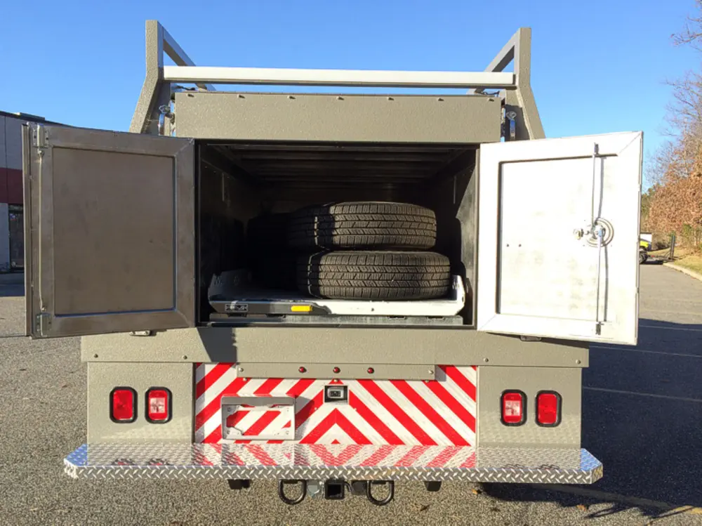 Exterior view of small fire truck showing cab, body compartments, and wheel/tire area.