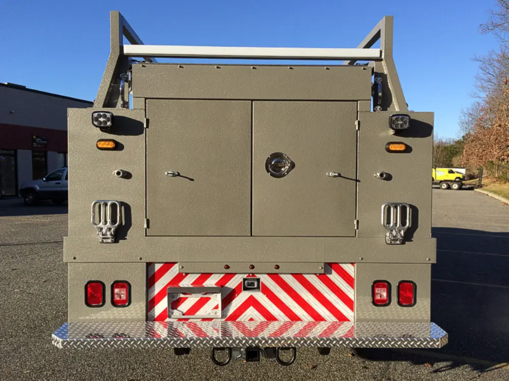 Exterior view of small fire truck showing cab, body compartments, and wheel/tire area.