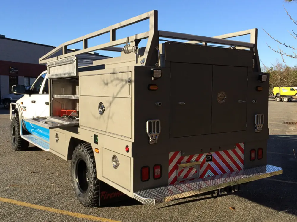 Exterior view of small fire truck showing cab, body compartments, and wheel/tire area.