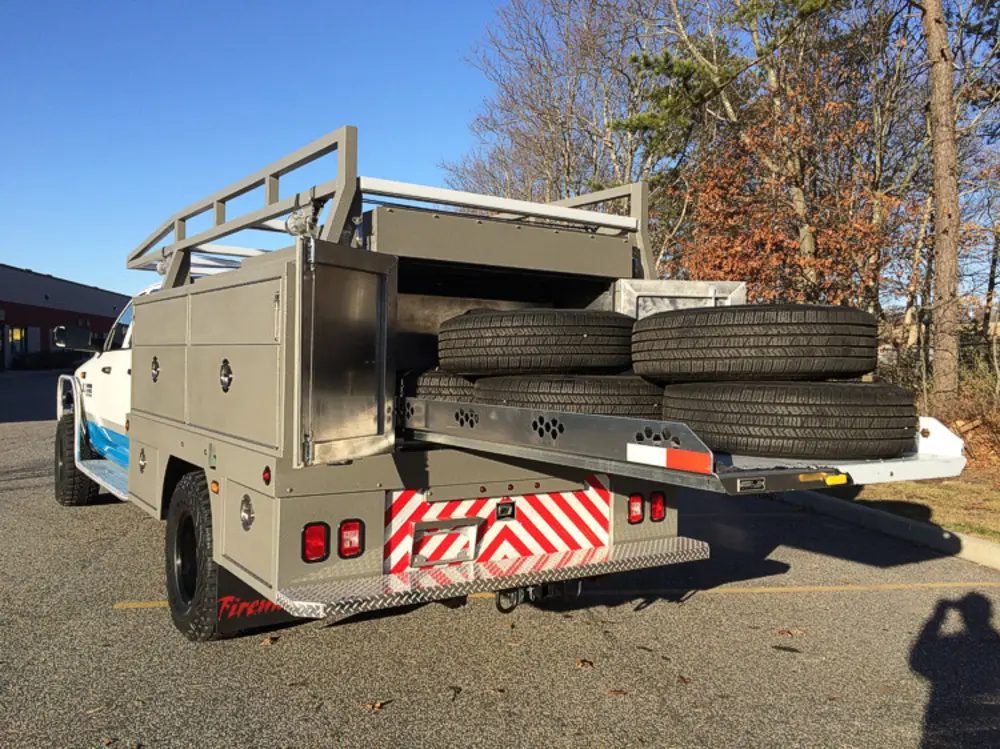 Exterior view of small fire truck showing cab, body compartments, and wheel/tire area.