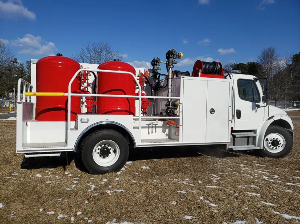 Exterior view of small fire truck showing cab, body compartments, and wheel/tire area.