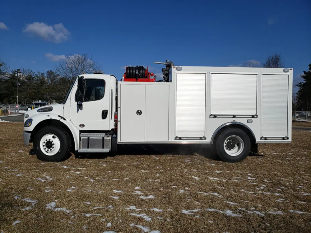 Exterior view of small fire truck showing cab, body compartments, and wheel/tire area.