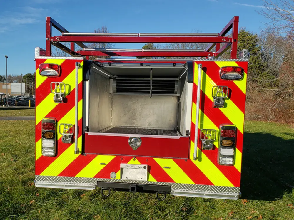 Exterior view of small fire truck showing cab, body compartments, and wheel/tire area.