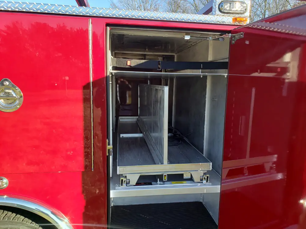 Exterior view of small fire truck showing cab, body compartments, and wheel/tire area.