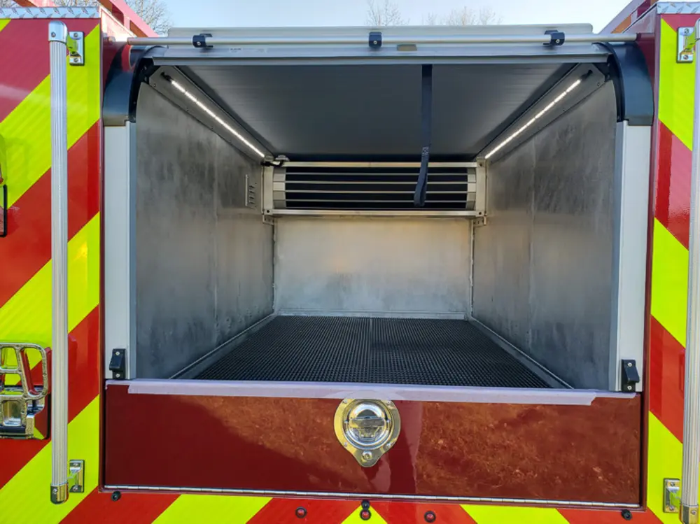 Exterior view of small fire truck showing cab, body compartments, and wheel/tire area.