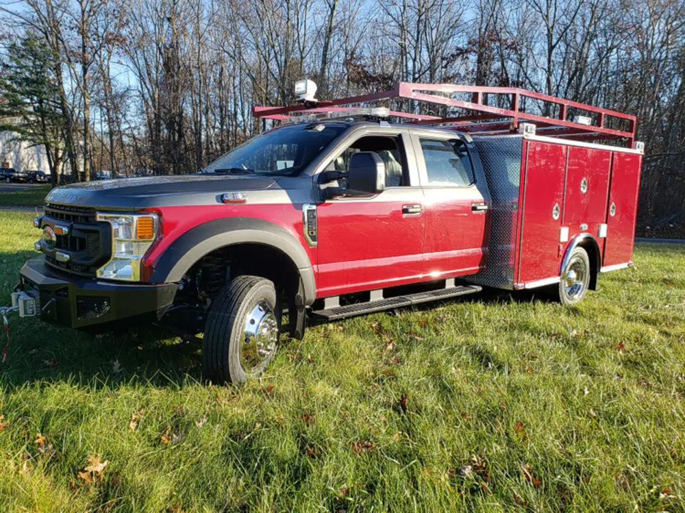 Exterior view of small fire truck showing cab, body compartments, and wheel/tire area.