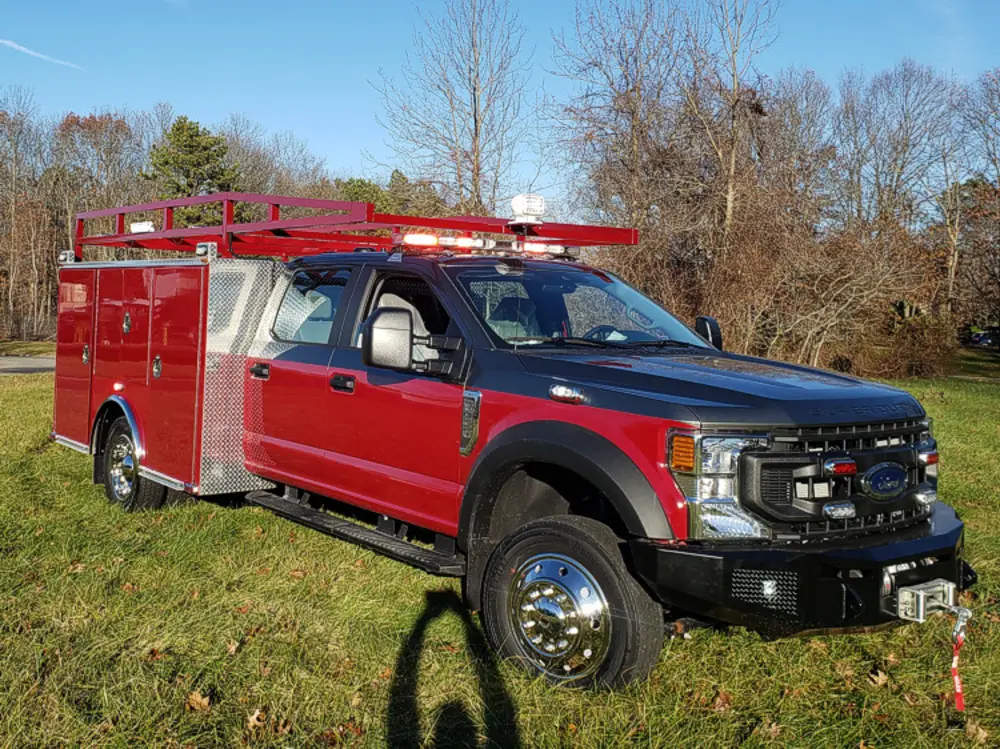 Exterior view of small fire truck showing cab, body compartments, and wheel/tire area.