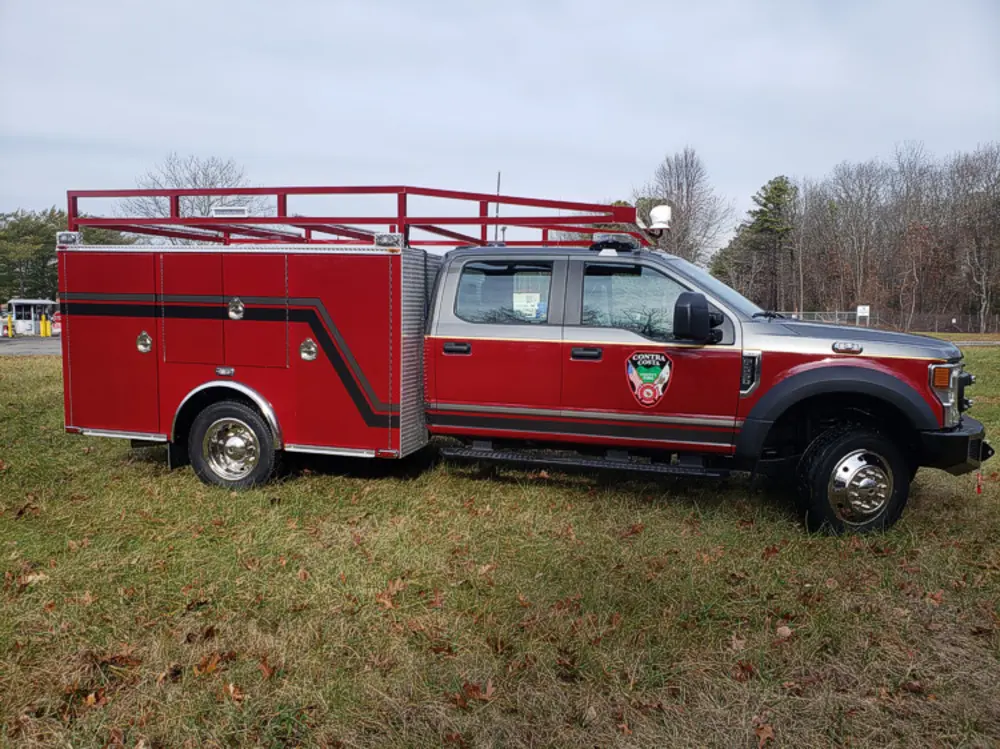 Exterior view of small fire truck showing cab, body compartments, and wheel/tire area.