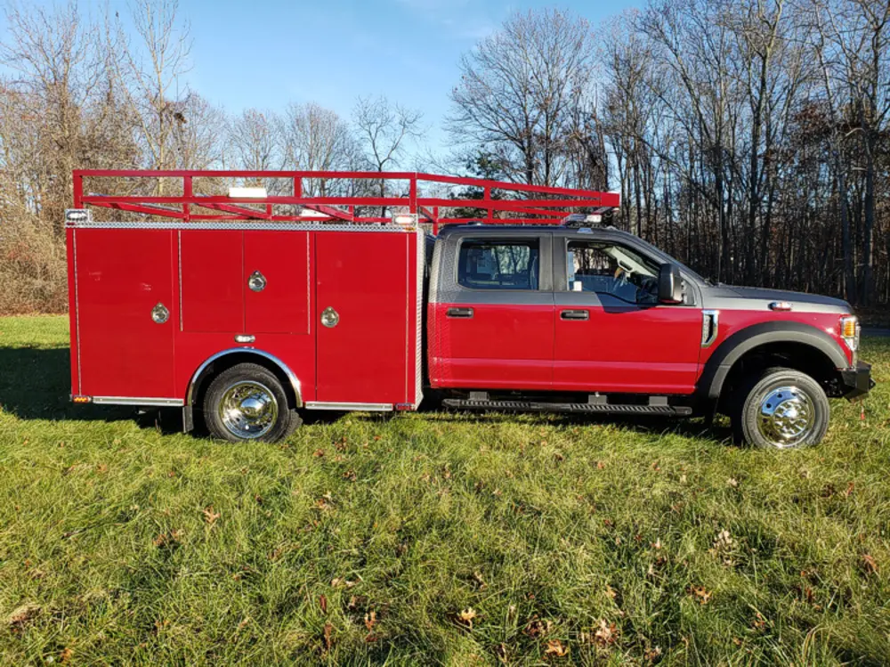 Exterior view of small fire truck showing cab, body compartments, and wheel/tire area.