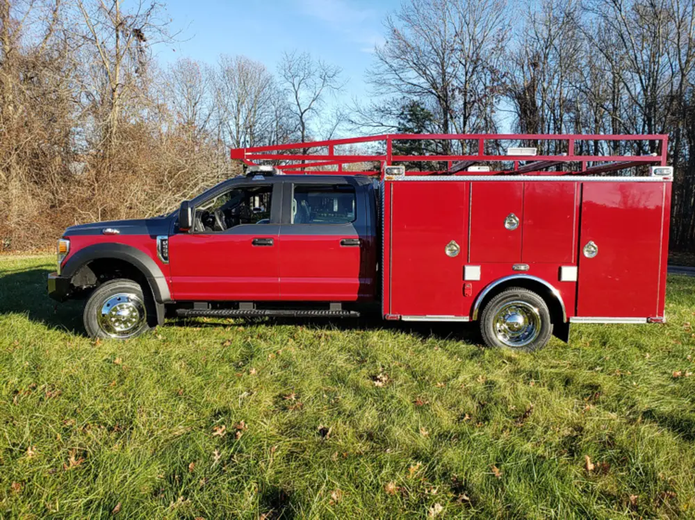 Exterior view of small fire truck showing cab, body compartments, and wheel/tire area.