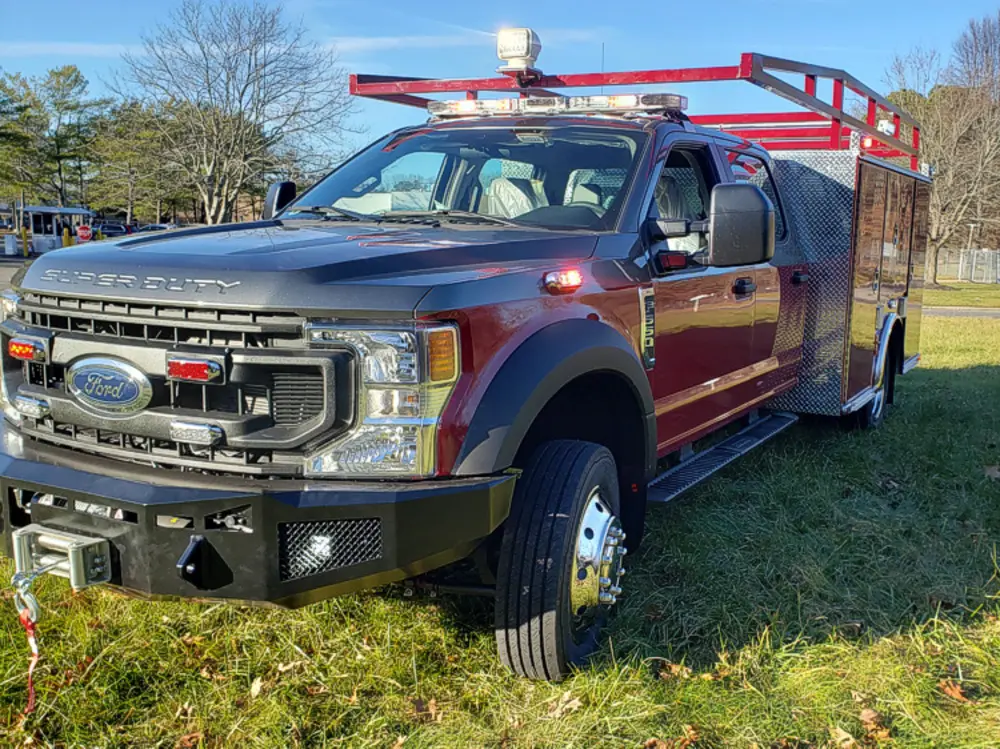 Exterior view of small fire truck showing cab, body compartments, and wheel/tire area.