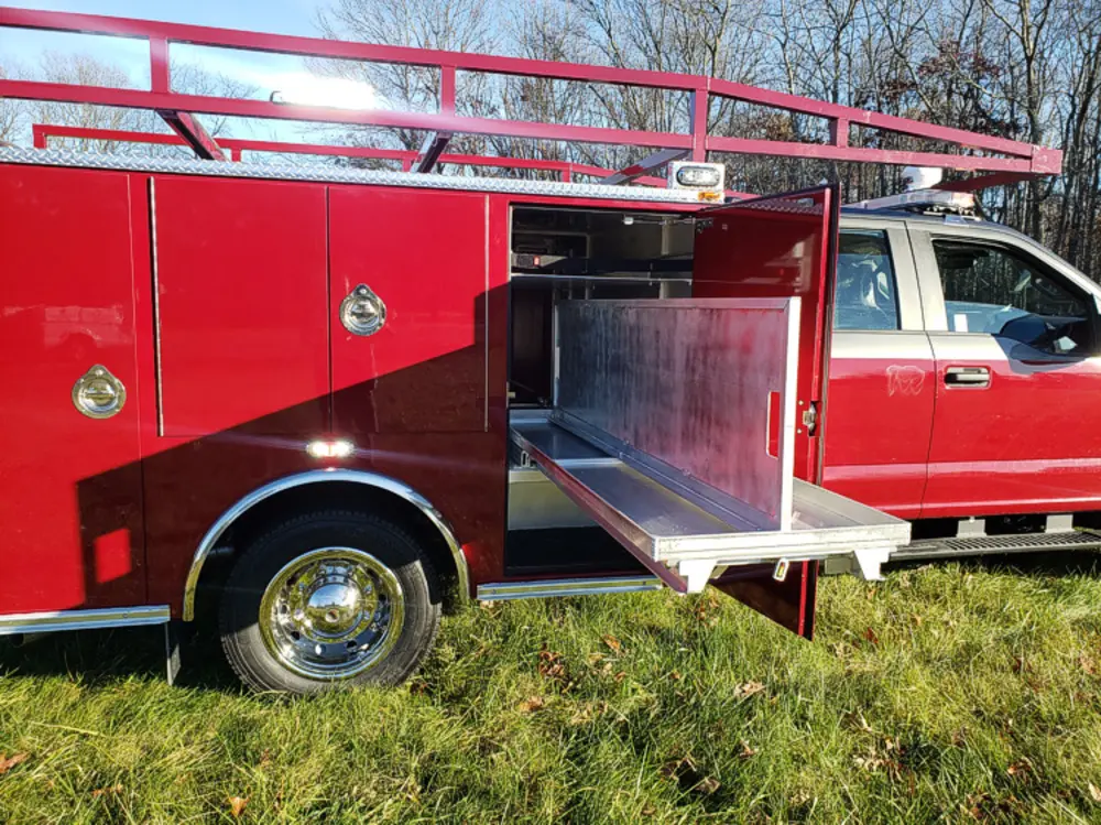 Exterior view of small fire truck showing cab, body compartments, and wheel/tire area.