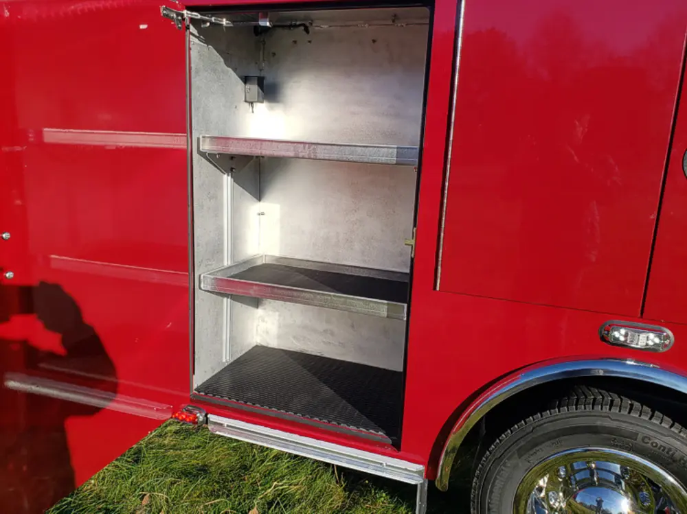 Exterior view of small fire truck showing cab, body compartments, and wheel/tire area.