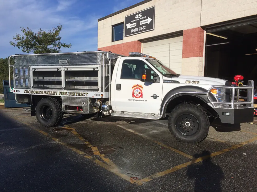 Exterior view of small fire truck showing cab, body compartments, and wheel/tire area.