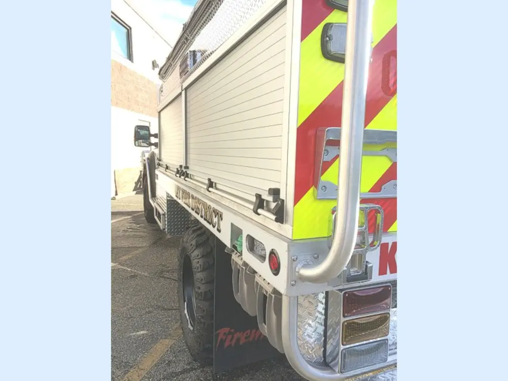 Exterior view of small fire truck showing cab, body compartments, and wheel/tire area.
