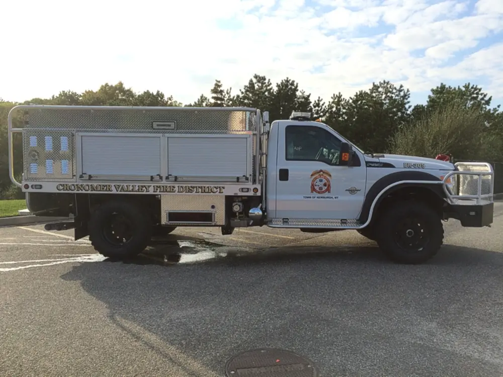 Exterior view of small fire truck showing cab, body compartments, and wheel/tire area.