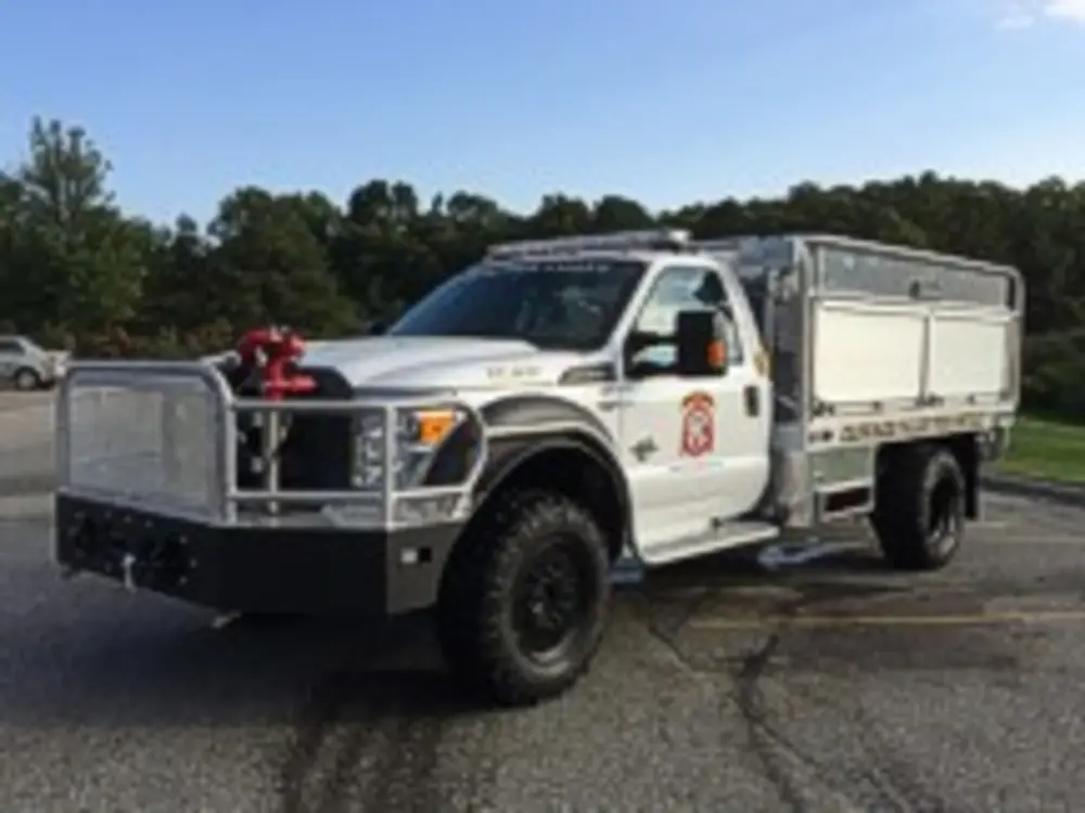 Exterior view of small fire truck showing cab, body compartments, and wheel/tire area.