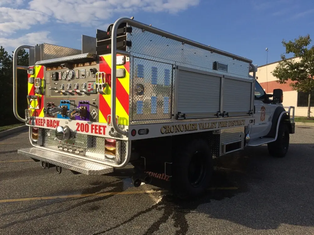 Exterior view of small fire truck showing cab, body compartments, and wheel/tire area.